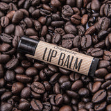 Black tube with brown label of Espresso Lip Balm on bed of coffee beand